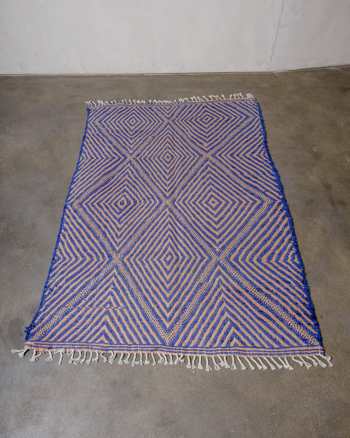 Blue and pink geometric patterned rug on a concrete floor.